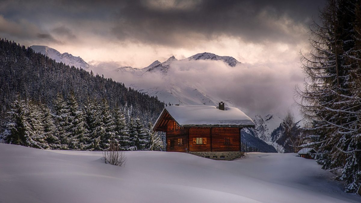 A small cabin shrouded by fog, amid snow, on a mountain
