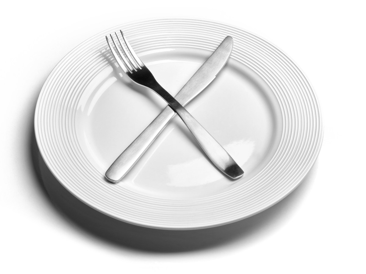 A clean, empty, white plate with a fork and knife atop it.