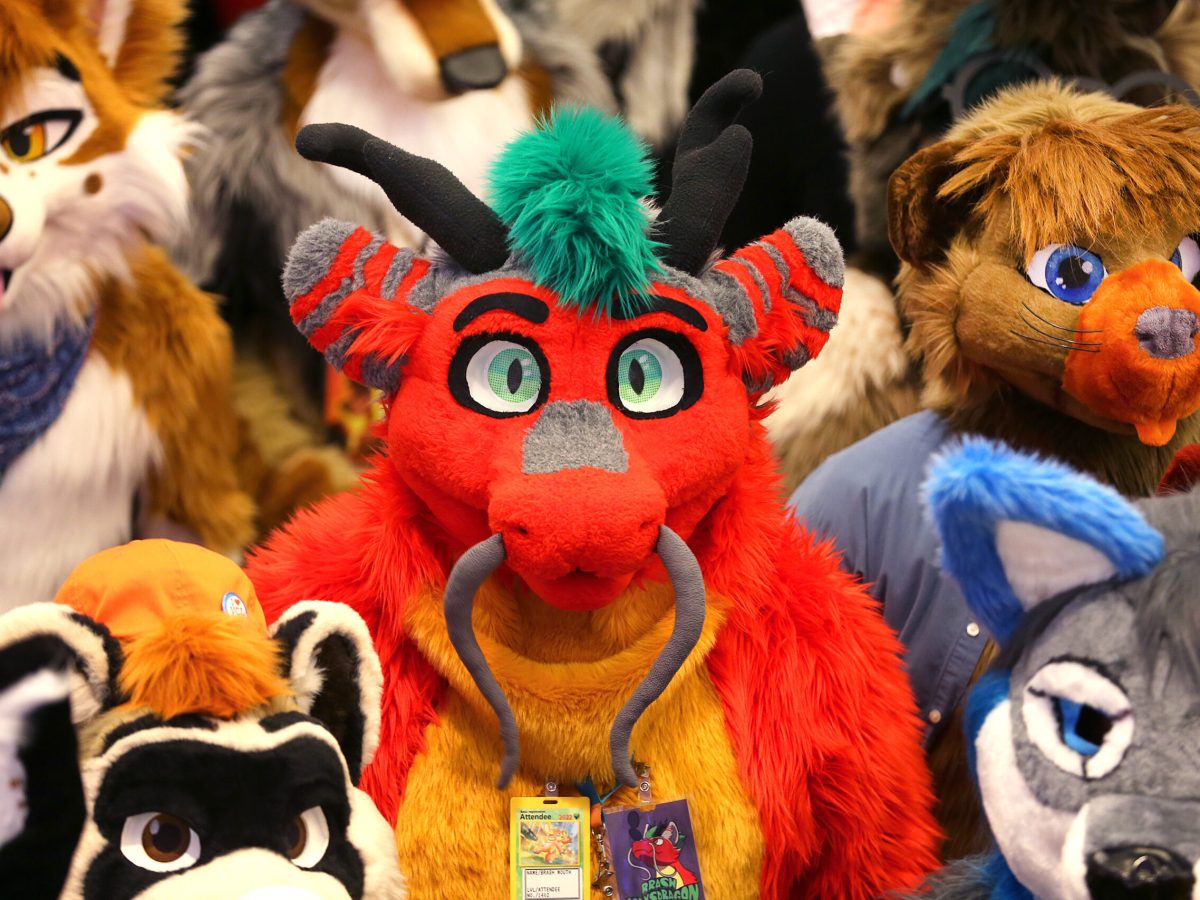 A person in a bright red furry bull costume, surrounded by others in furry animal cosplay.