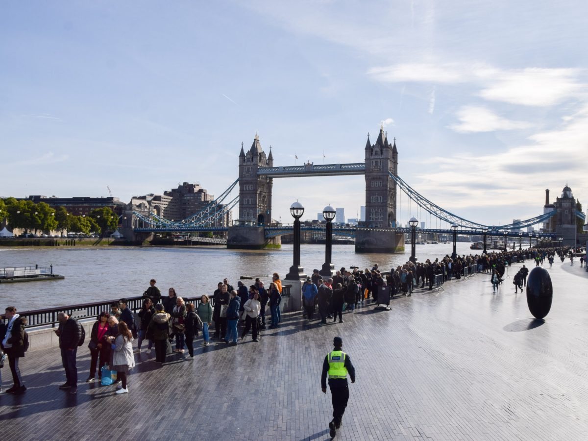 A long line of people stand near the Tower Bridge in London