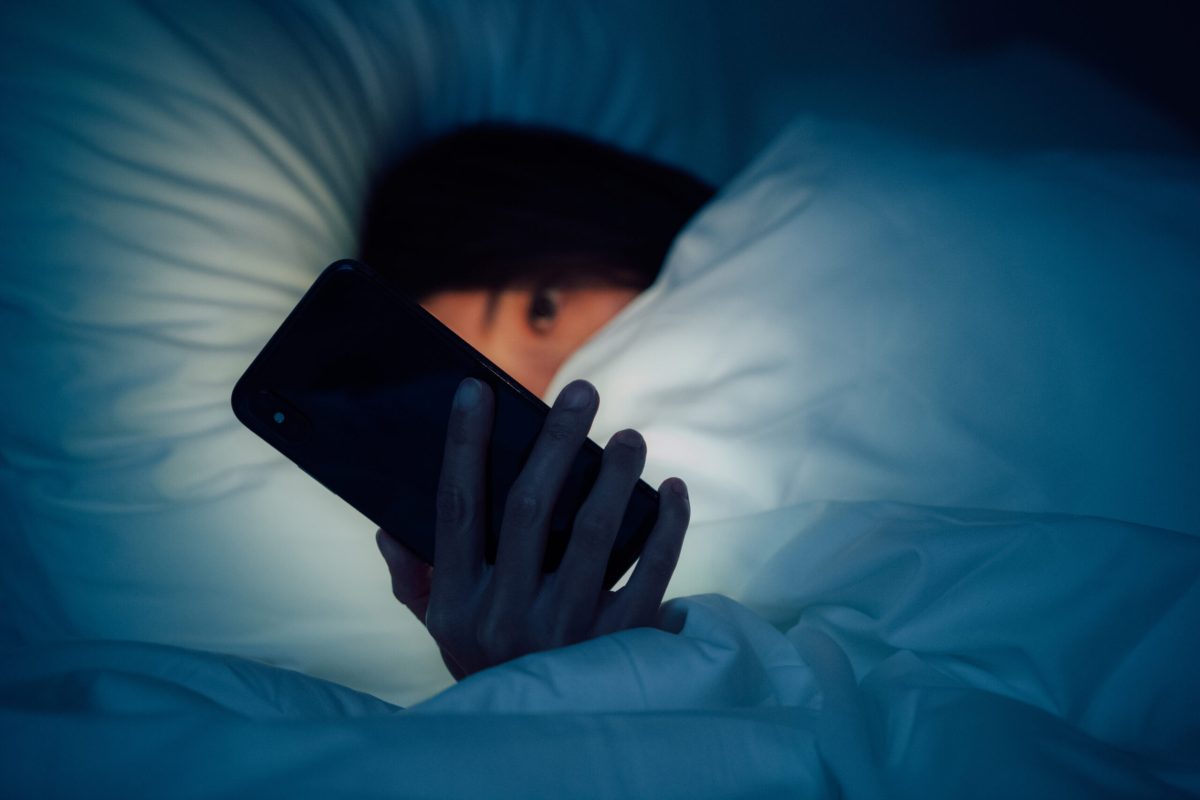 Woman hiding under the blanket, chatting and surfing the internet with smart phone at late night on bed.