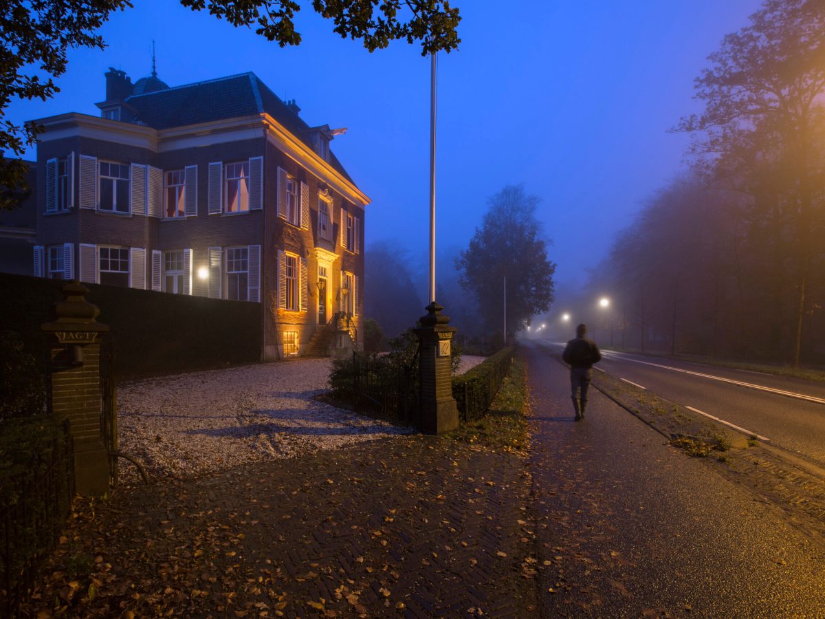 On a misty evening, a man walks along a quiet Dutch street
