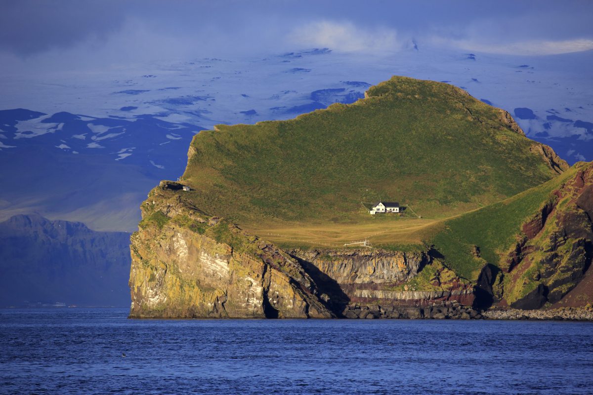 A white house perches on a craggy island, surrounded by water.