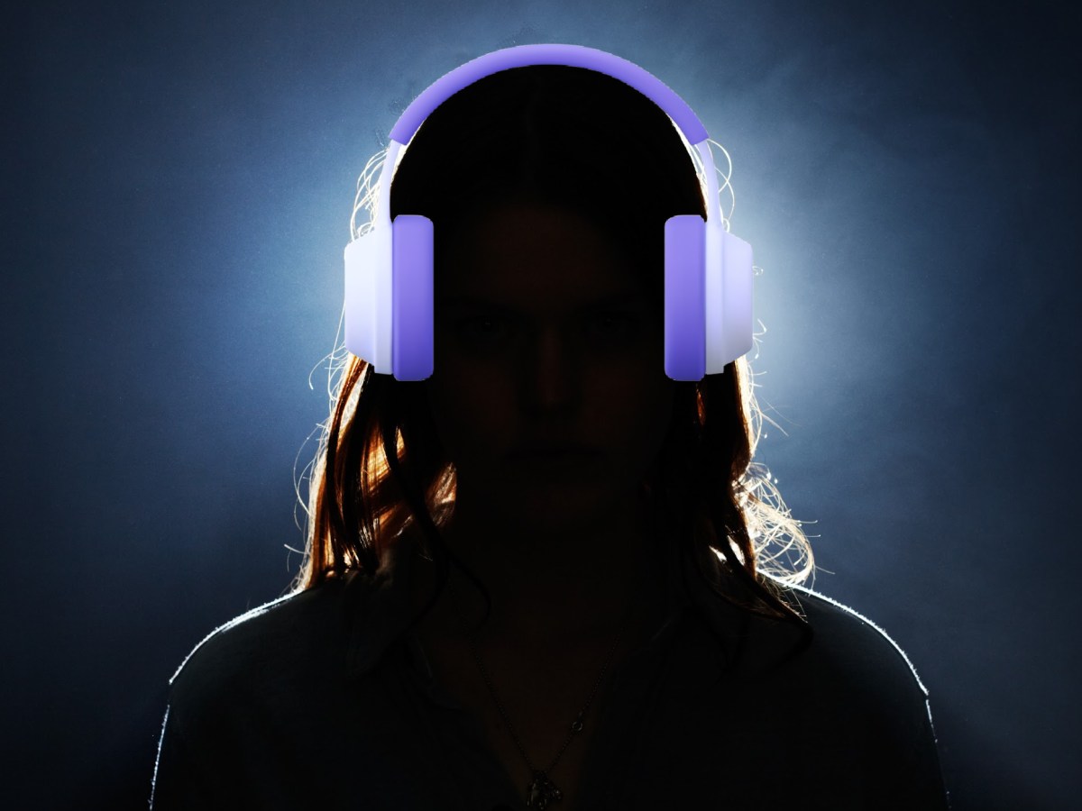 A young woman wearing over-ear headphones, seen from behind, backlit and in silhouette.