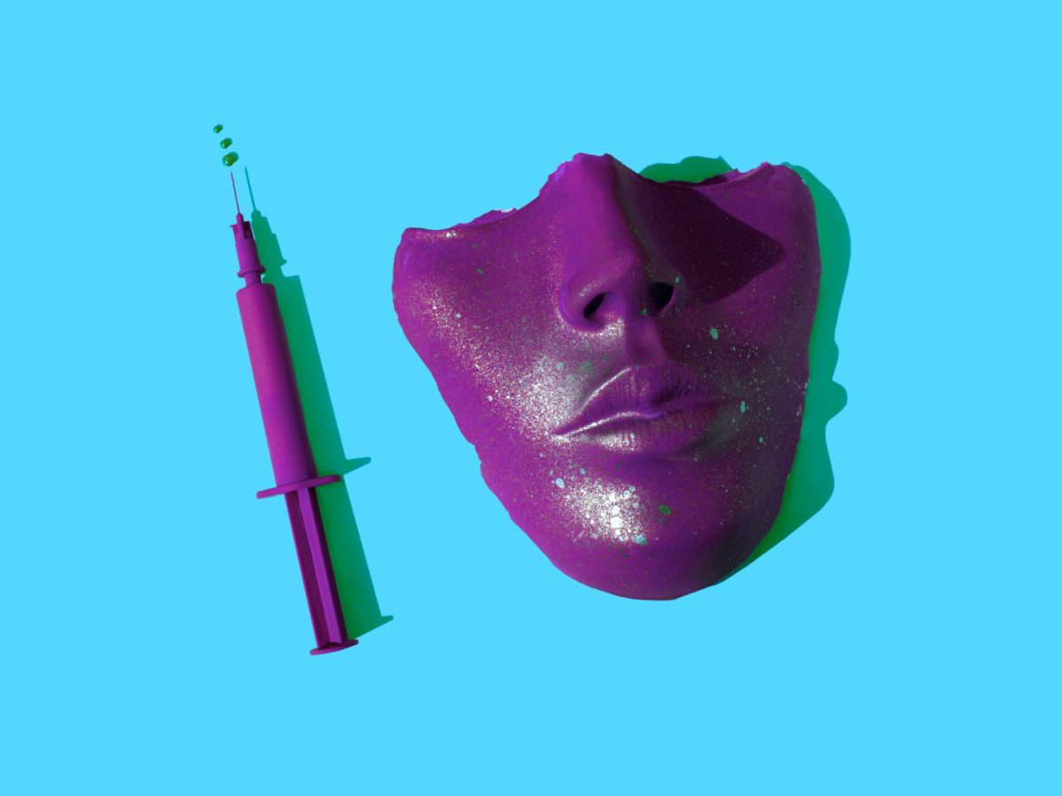 Half a plaster mask of a human face and a syringe — both magenta — sit against a bright blue background