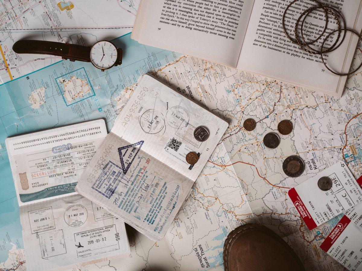 Passport and travel documents, a watch, an open book, and coins on top of paper maps