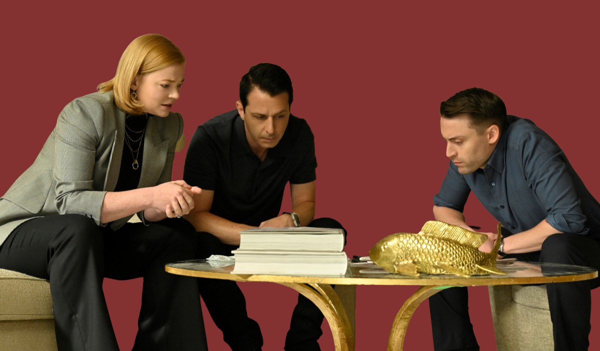 Three characters from the HBO show "Succession" — Shiv, Kendall, and Roman Roy — sit around a table with serious looks on their faces.