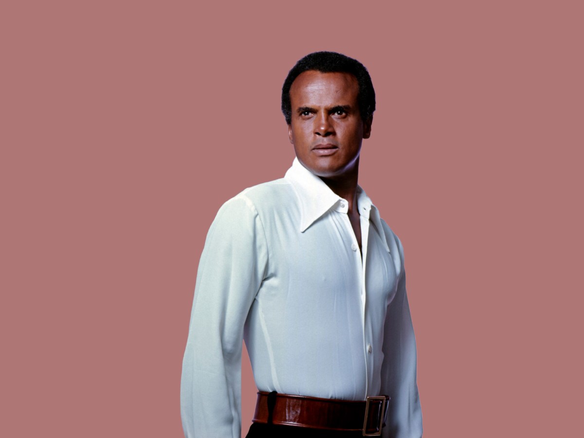 Harry Belafonte stands in three-quarter profile against a mauve background, wearing a white shirt and with a proud expression.