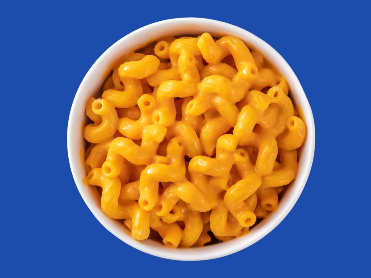 A bowl of bright orange macaroni and cheese, photographed from above, against a deep blue background