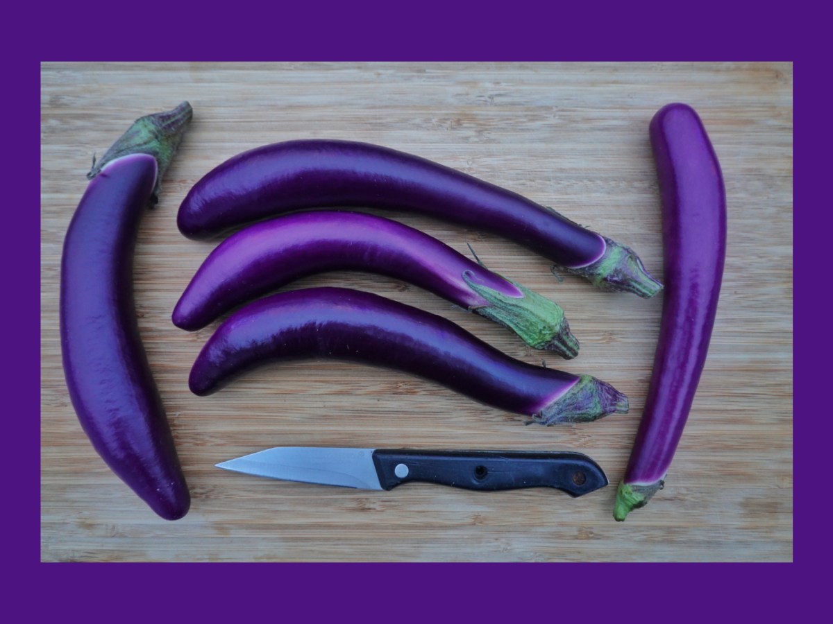 Japanese eggplants lie next to a knife on a cutting board.