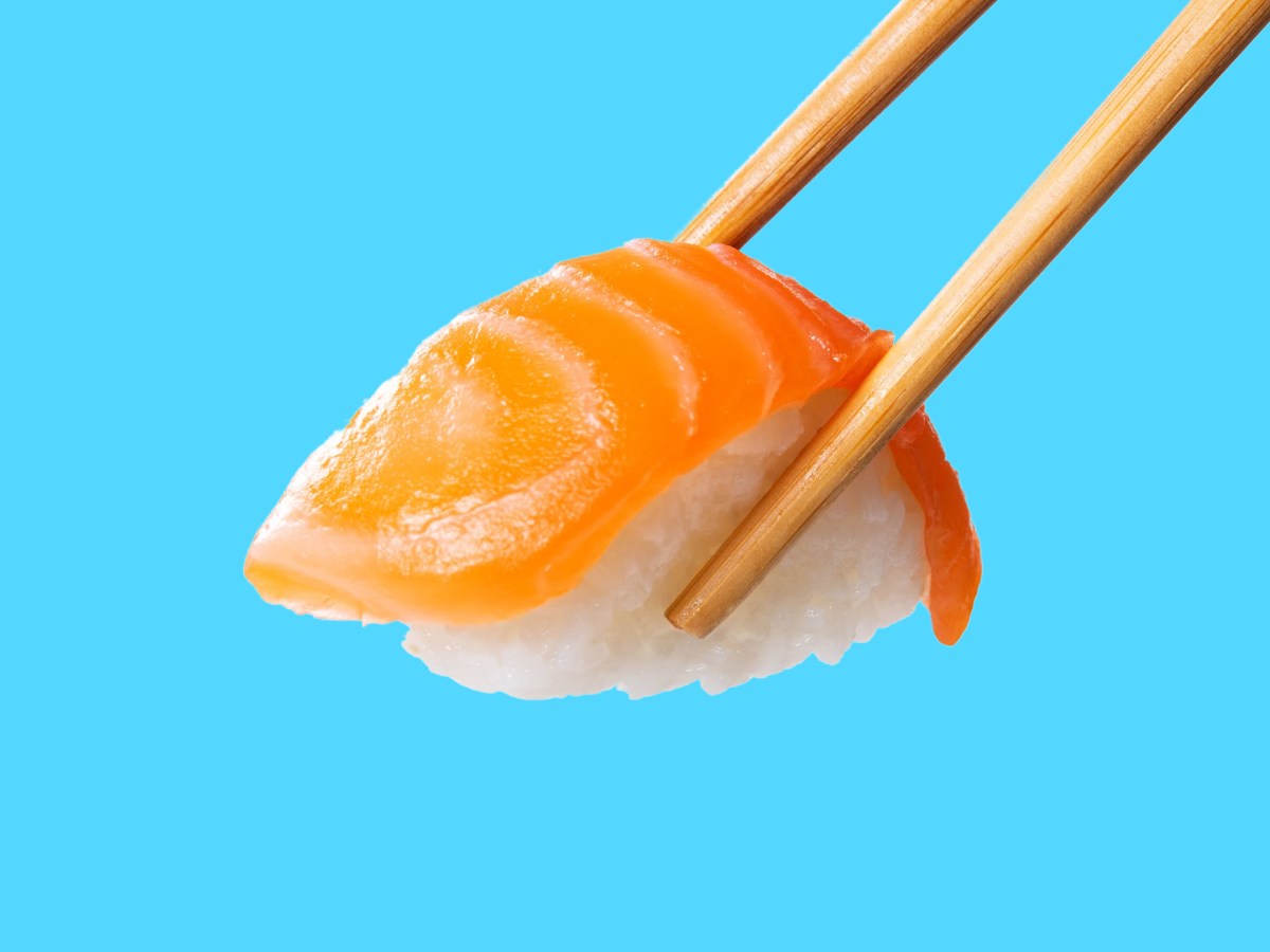 A piece of salmon nigiri, held by chopsticks, against a bright blue background