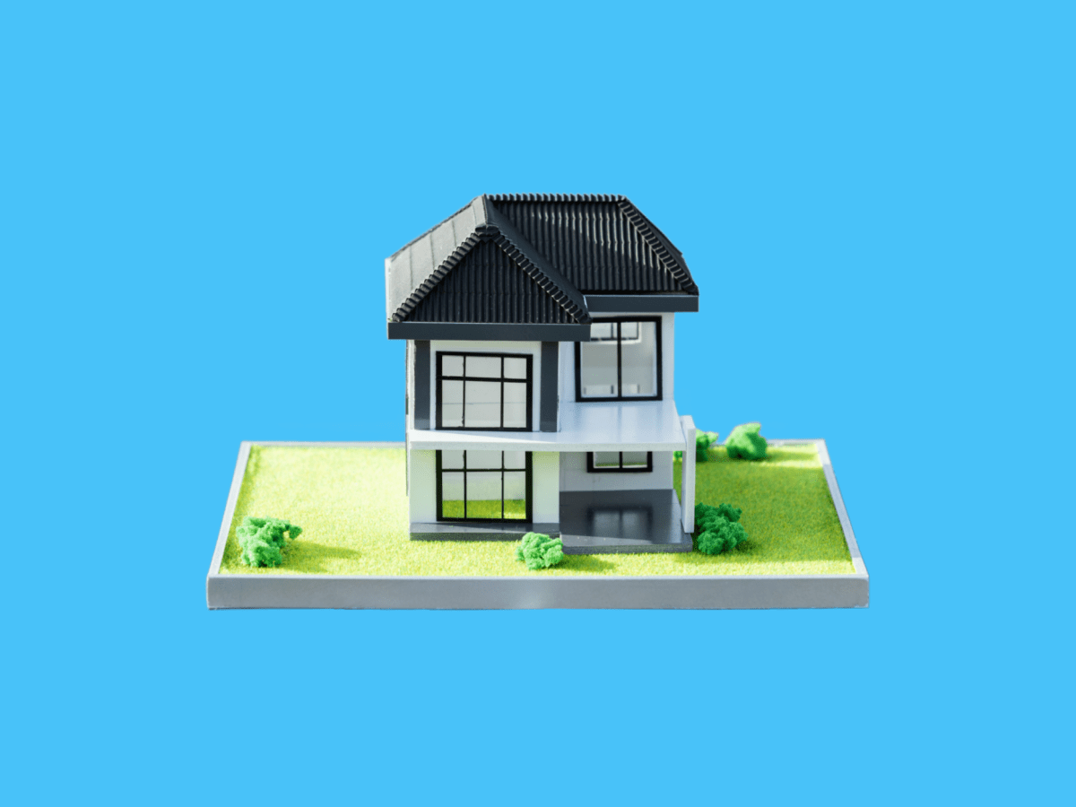 A miniature house sits on a small base against a sky-blue background