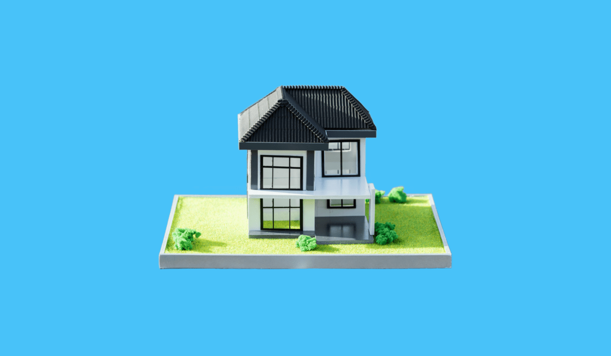 A miniature house sits on a small base against a sky-blue background