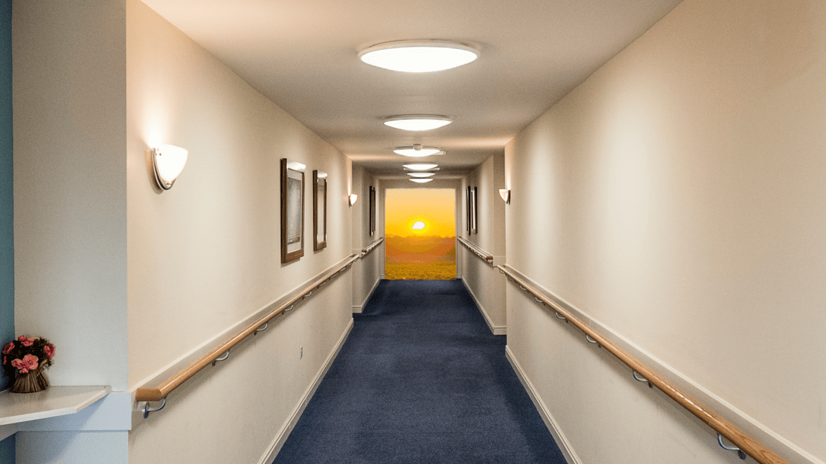 Photo of a long carpeted hallway with handrails along each wall. At the end, a sunset.